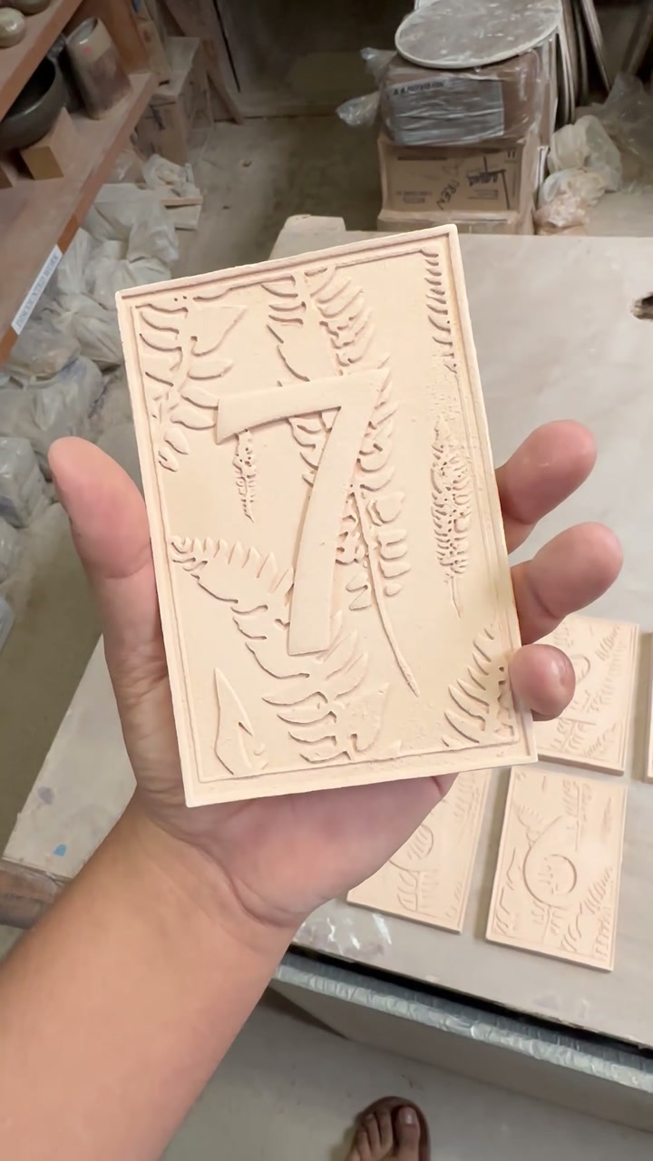 Holding the bisque-fired number seven tile, with raised fern leaves and a double-rule border